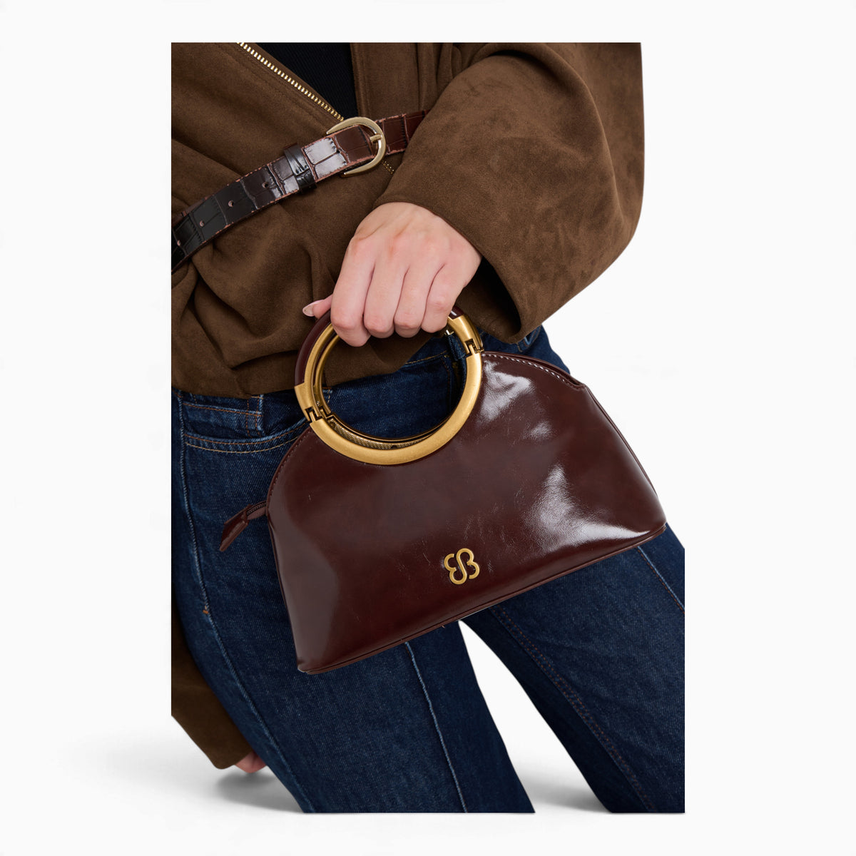 Wine ring handle crossbody bag held by its gold ring handle, close-up