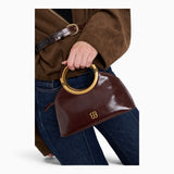 Wine ring handle crossbody bag held by its gold ring handle, close-up