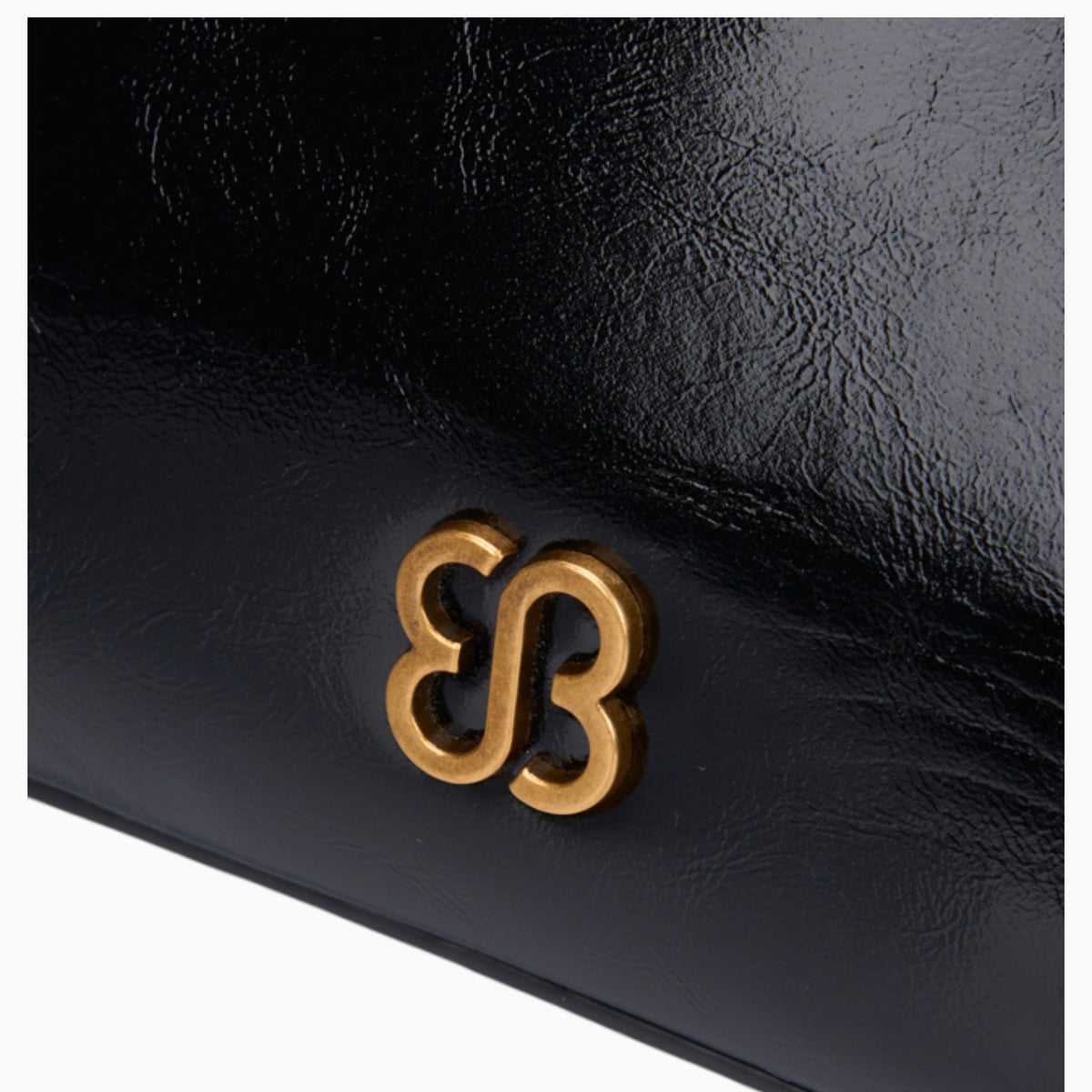 Black ring handle crossbody bag, close-up of the gold-tone logo on the glossy finish