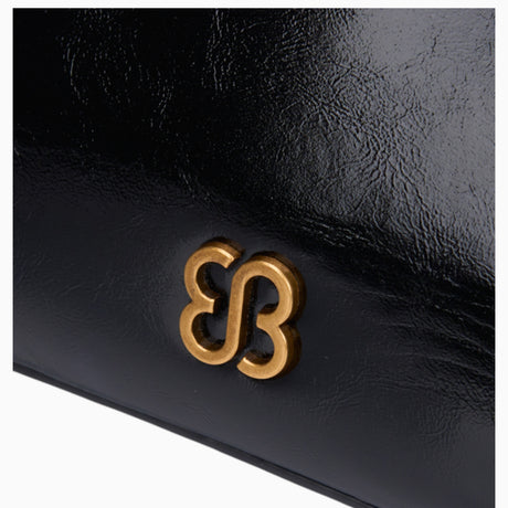 Black ring handle crossbody bag, close-up of the gold-tone logo on the glossy finish